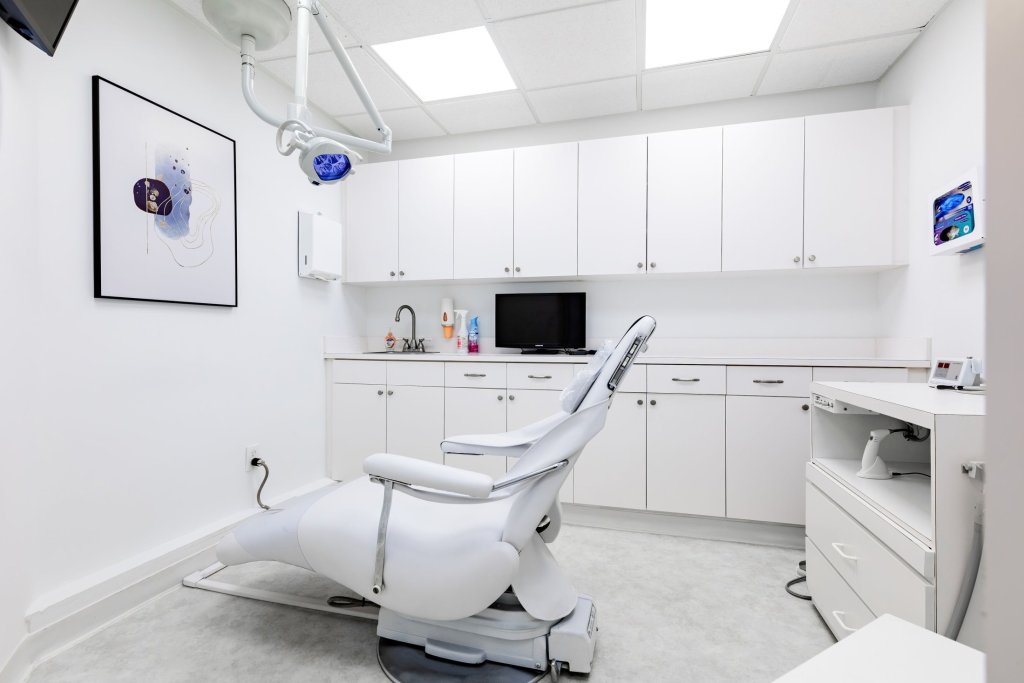 Modern white dental operatory with patient chair, white cabinetry, wall-mounted artwork, and clinical equipment in bright sterile environment