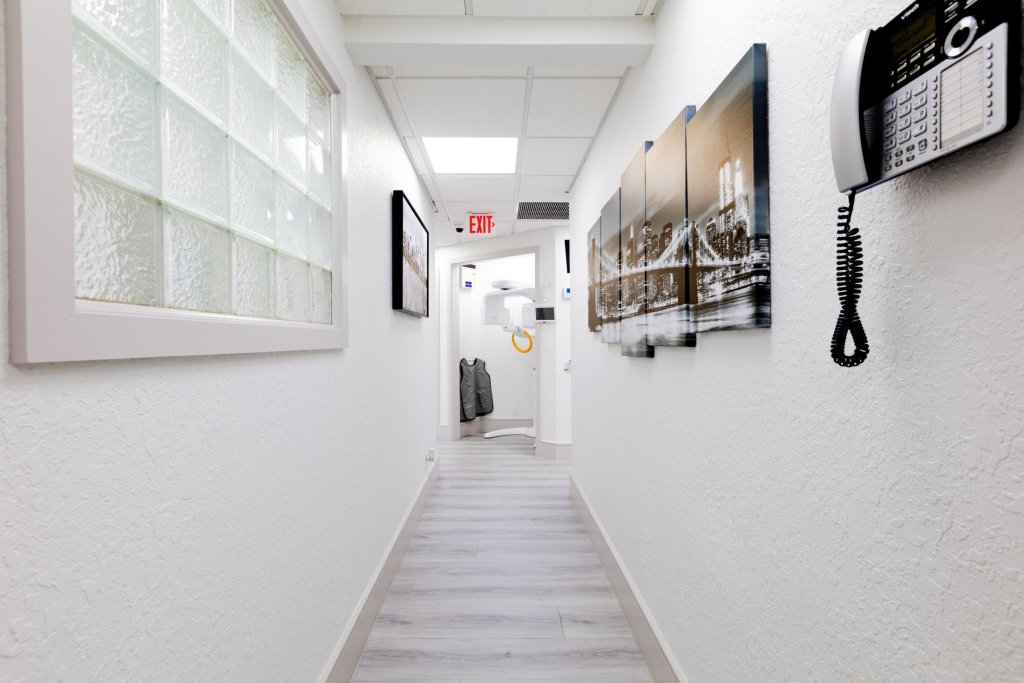 Clean white hallway with light wood-style flooring, framed artwork on walls, glass block window feature, and wall-mounted telephone system