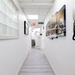 Clean white hallway with light wood-style flooring, framed artwork on walls, glass block window feature, and wall-mounted telephone system