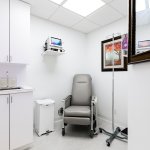 Compact dental operatory with grey patient chair, white cabinetry, wall-mounted equipment, mirror, and skylight in clean modern design