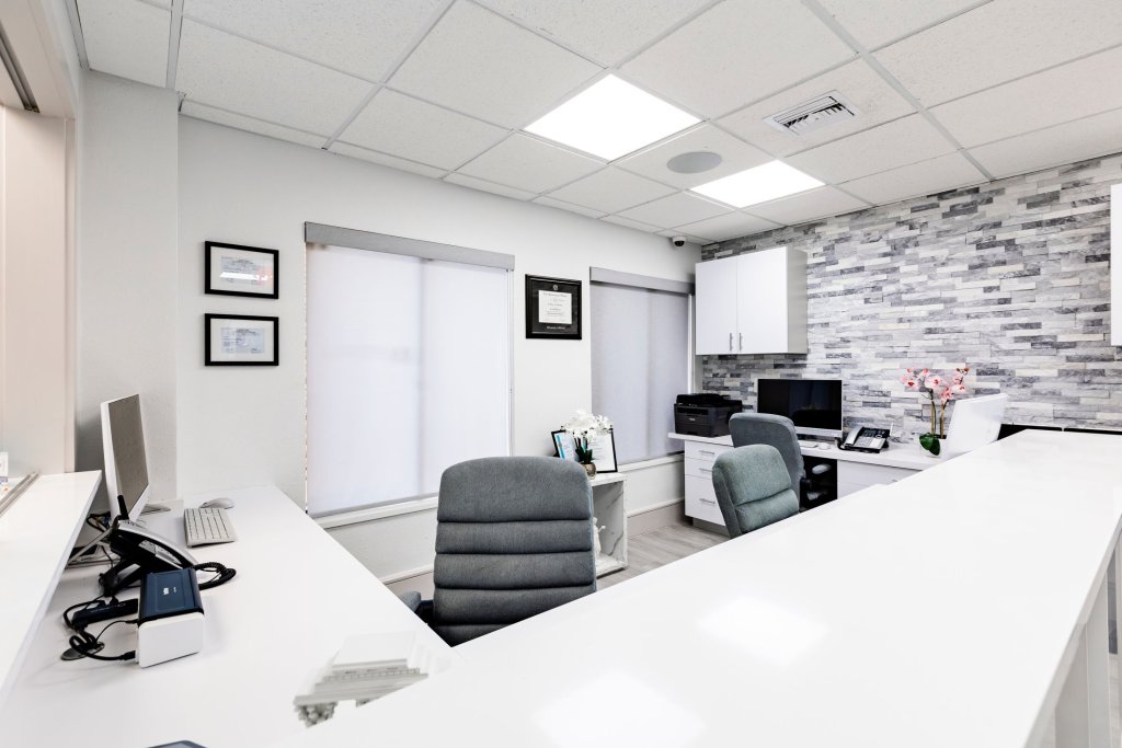 Reception area with long white desk, computer workstations, grey office chairs, and textured stone accent wall