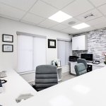Reception area with long white desk, computer workstations, grey office chairs, and textured stone accent wall